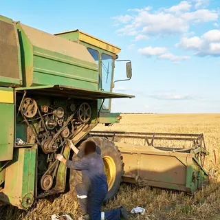 Механик обслуживает приводные ремни и шкивы зерноуборочного комбайна в поле